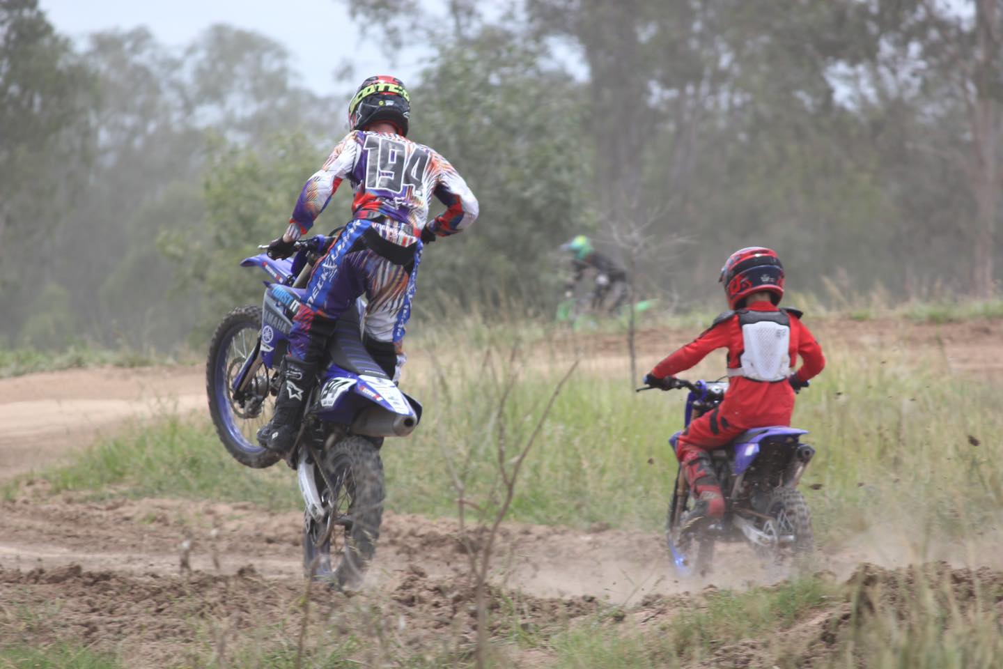 two people on dirt bikes, one popping a wheelie
